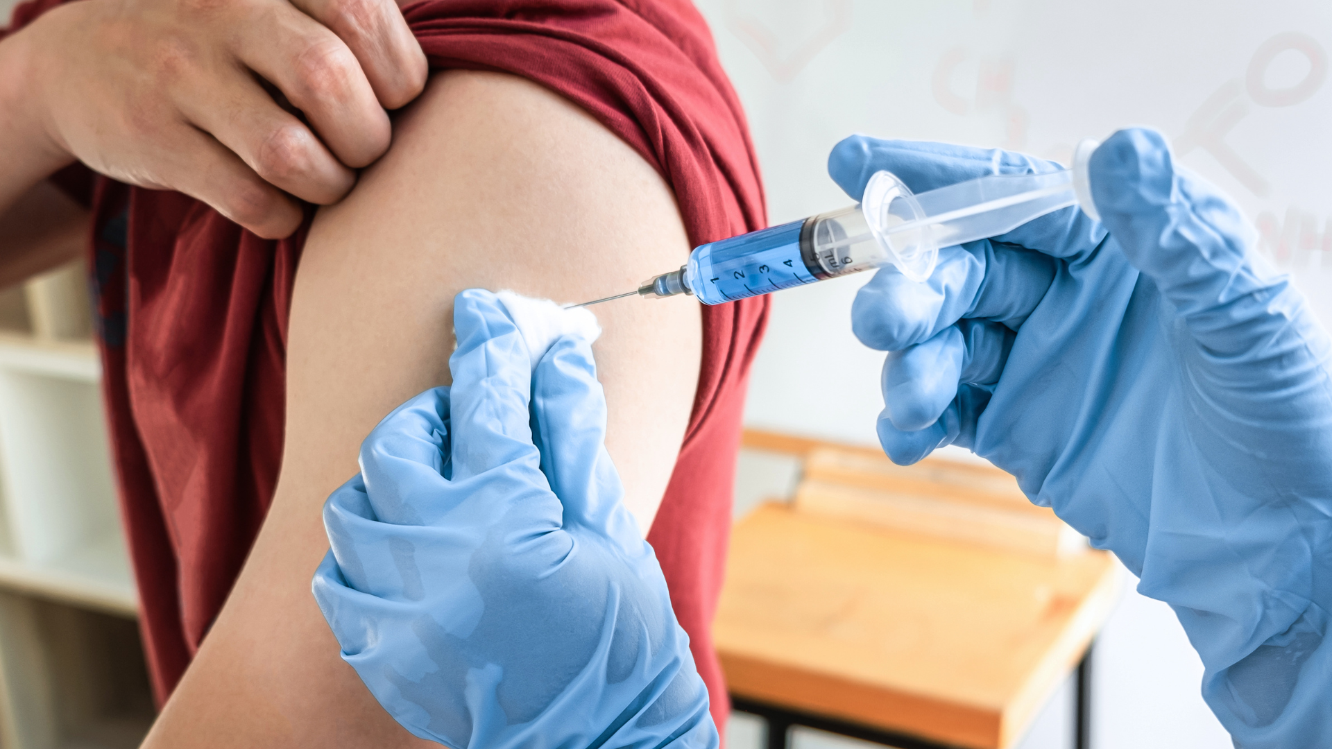 A medical professional wearing blue gloves administers an injection into a patient’s upper arm.