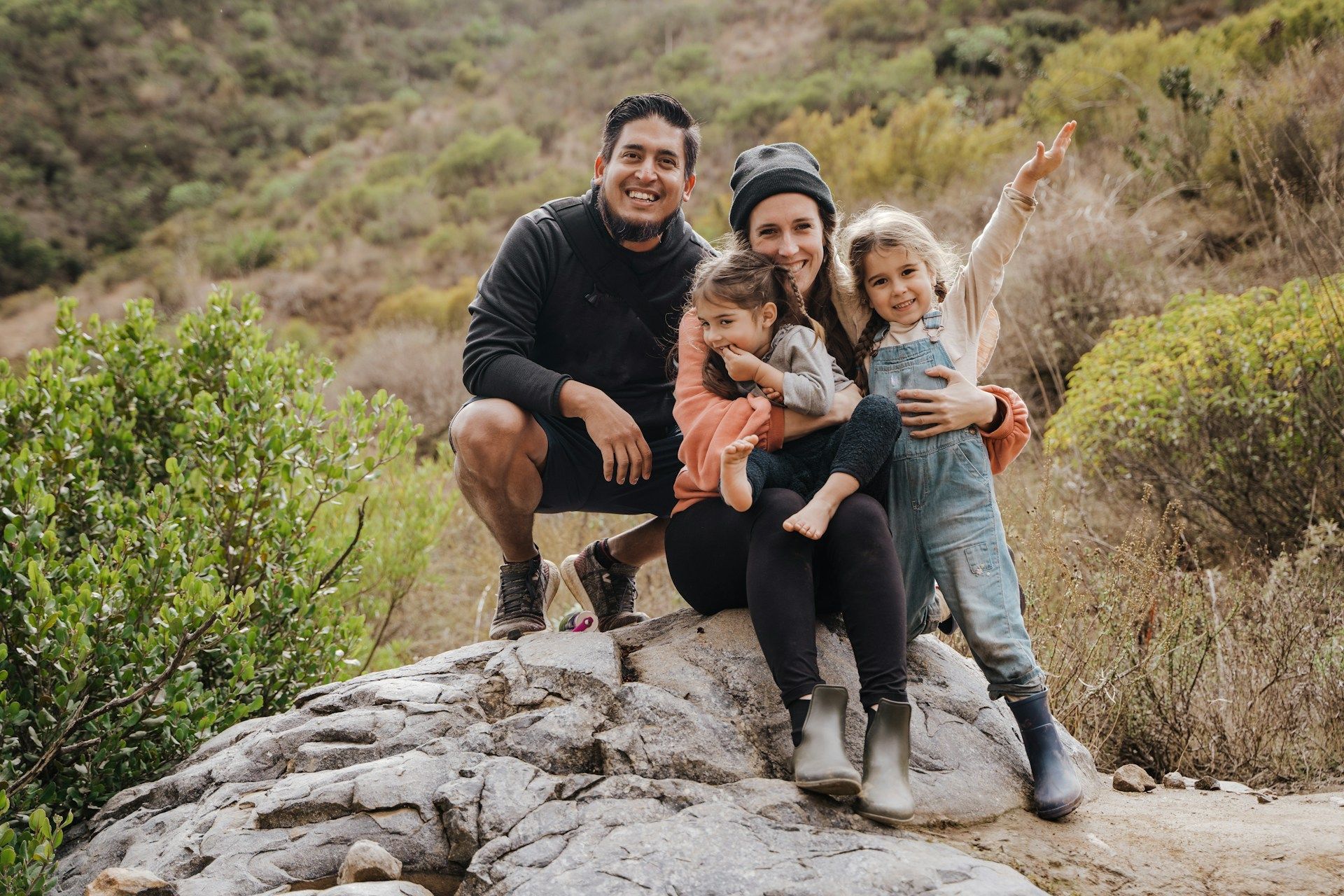 A family is sitting on top of a rock in the woods.