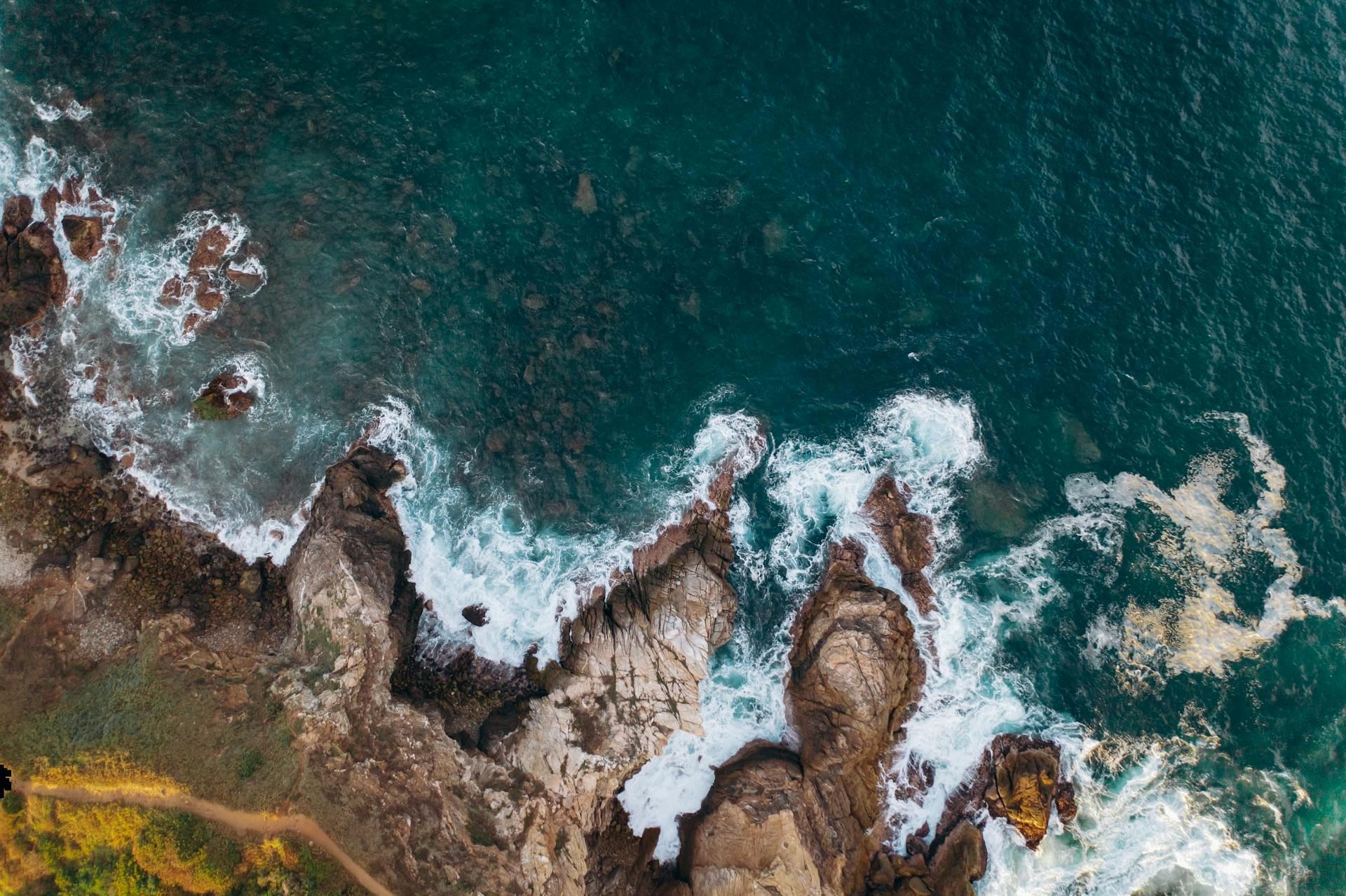 An aerial view of a rocky shoreline with waves crashing against the rocks.