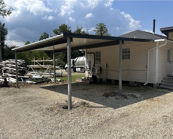 Carport next to a building on gravel. Steel frame and white metal roof. Cloudy sky.