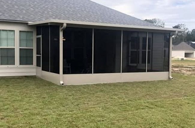 Screened-in patio extension attached to a tan house with windows, overlooking a grassy yard.
