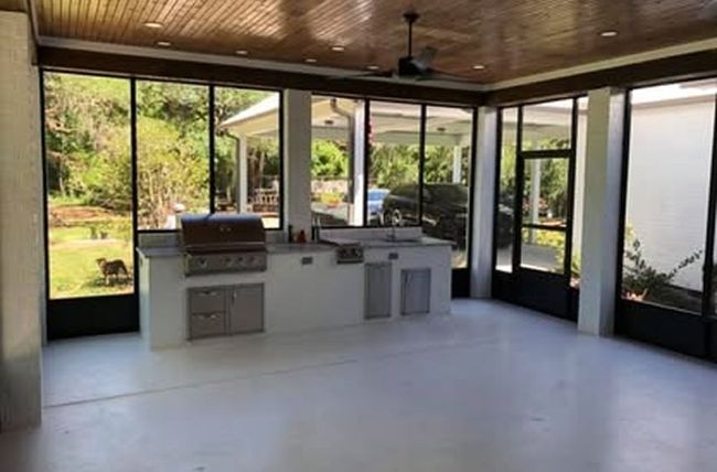 Outdoor kitchen with grill, sink, and cabinets, enclosed by windows.