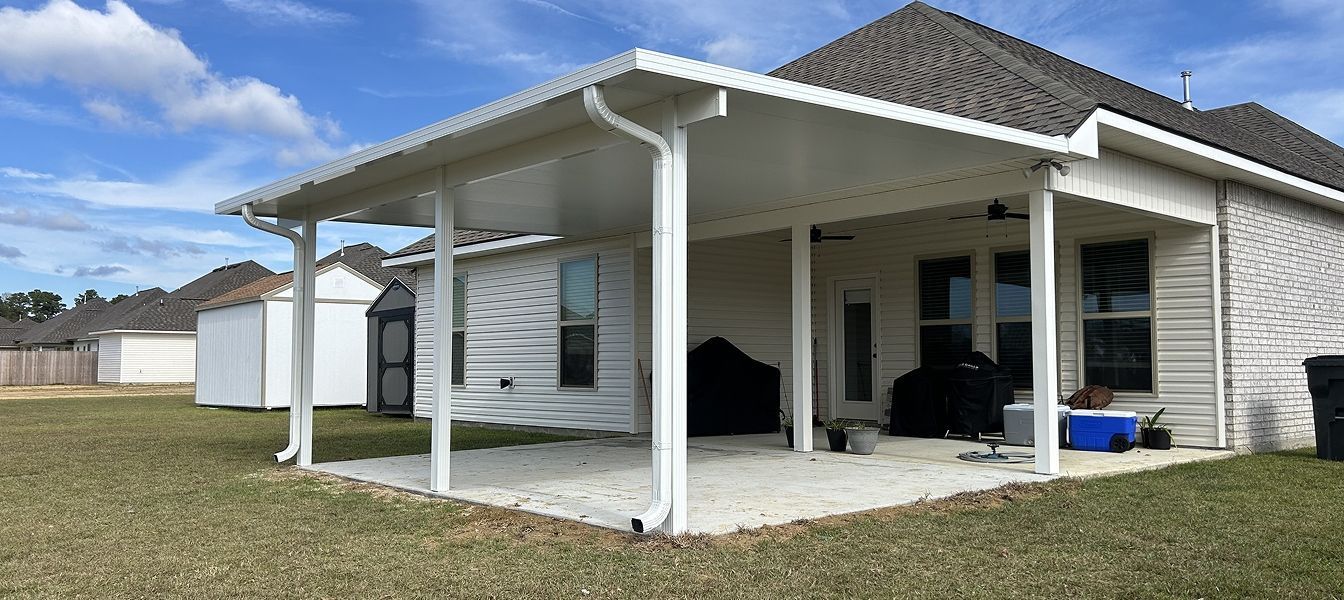 A white patio cover extends from a house, over a concrete patio. Grassy yard surrounds.