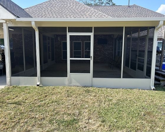 Screened-in porch attached to a house; beige trim and roof, gray brick interior, green lawn.