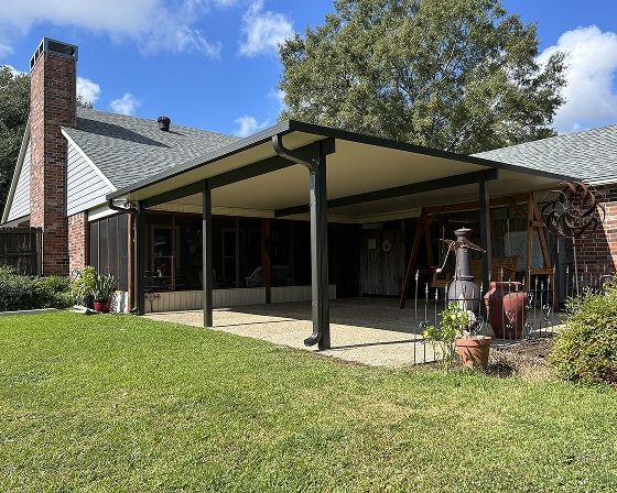 Backyard patio with a tan roof and dark gray support beams. A brick chimney and house are also visible.