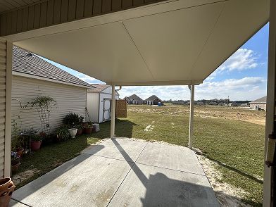 Patio with a white roof, concrete floor, and view of a yard and houses under a blue sky.