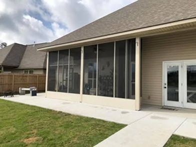 Screened porch attached to a tan house with a concrete patio and green lawn.