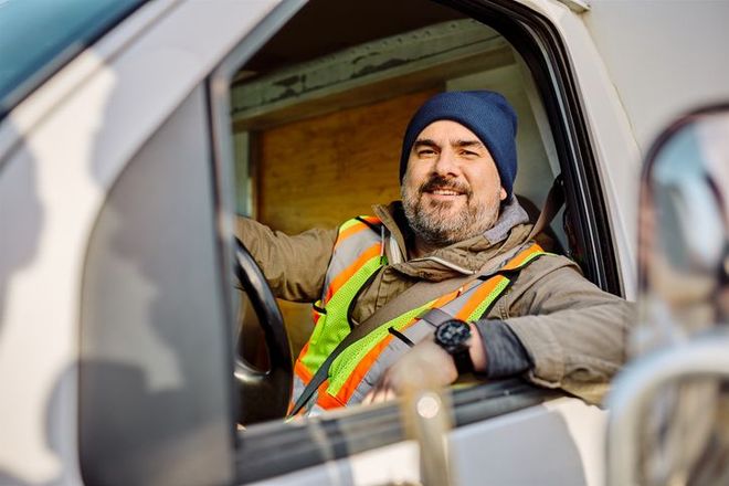 Happy truck driver sitting in vehicle cabin and looking at camera