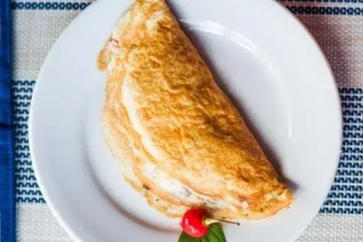 Um prato branco coberto com uma omelete e uma cereja sobre uma mesa.