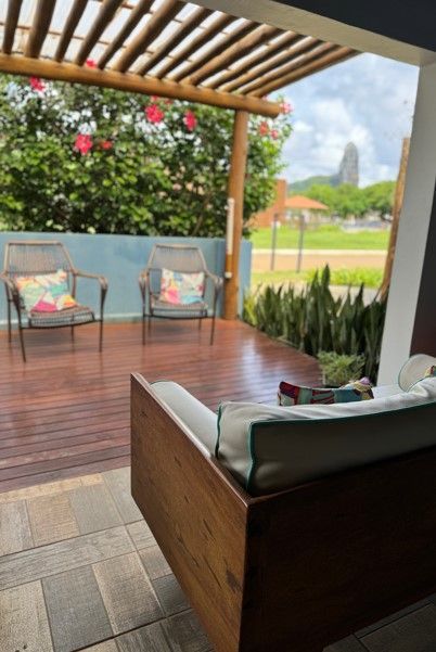 Um deck de madeira com um sofá e cadeiras sob uma pérgola