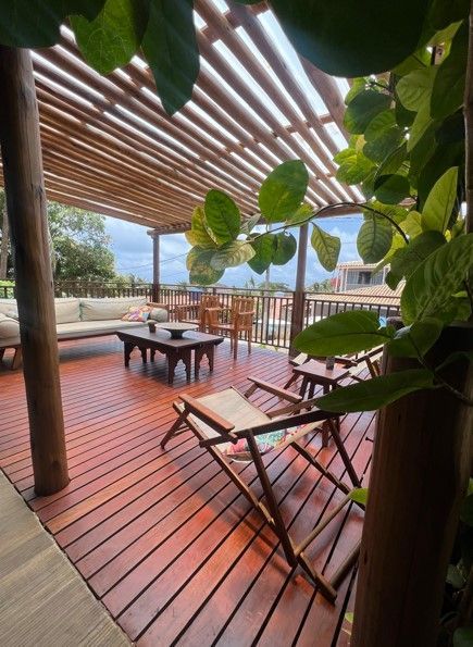 Um deck de madeira com cadeiras e mesas sob uma pérgola