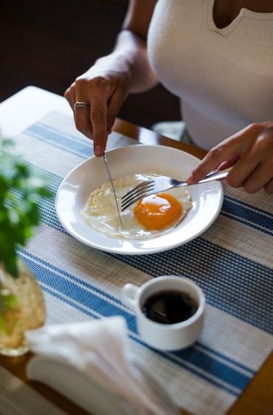 Uma mulher está cortando um ovo em um prato com um garfo.