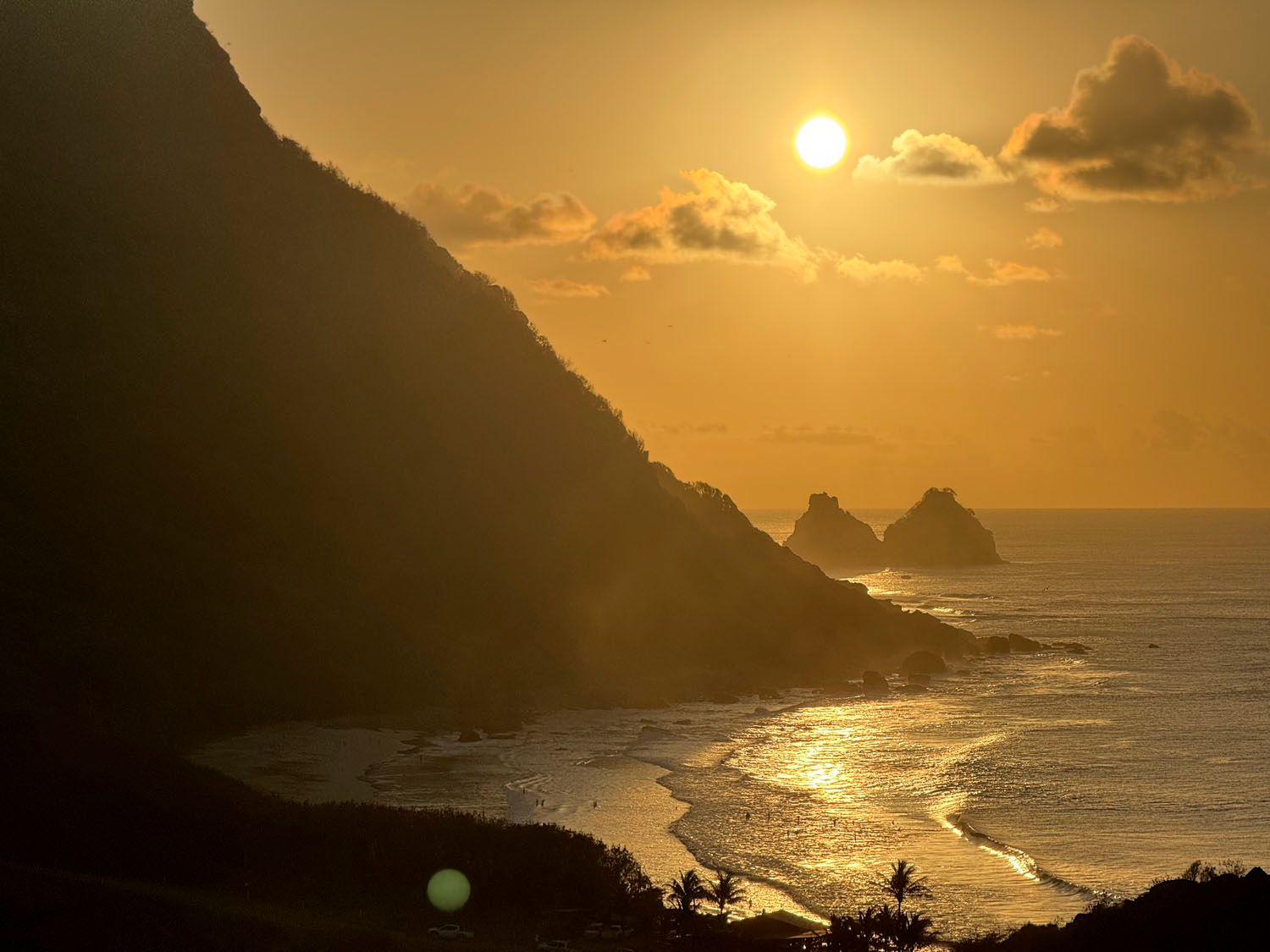 O sol está se pondo sobre o oceano com montanhas ao fundo.