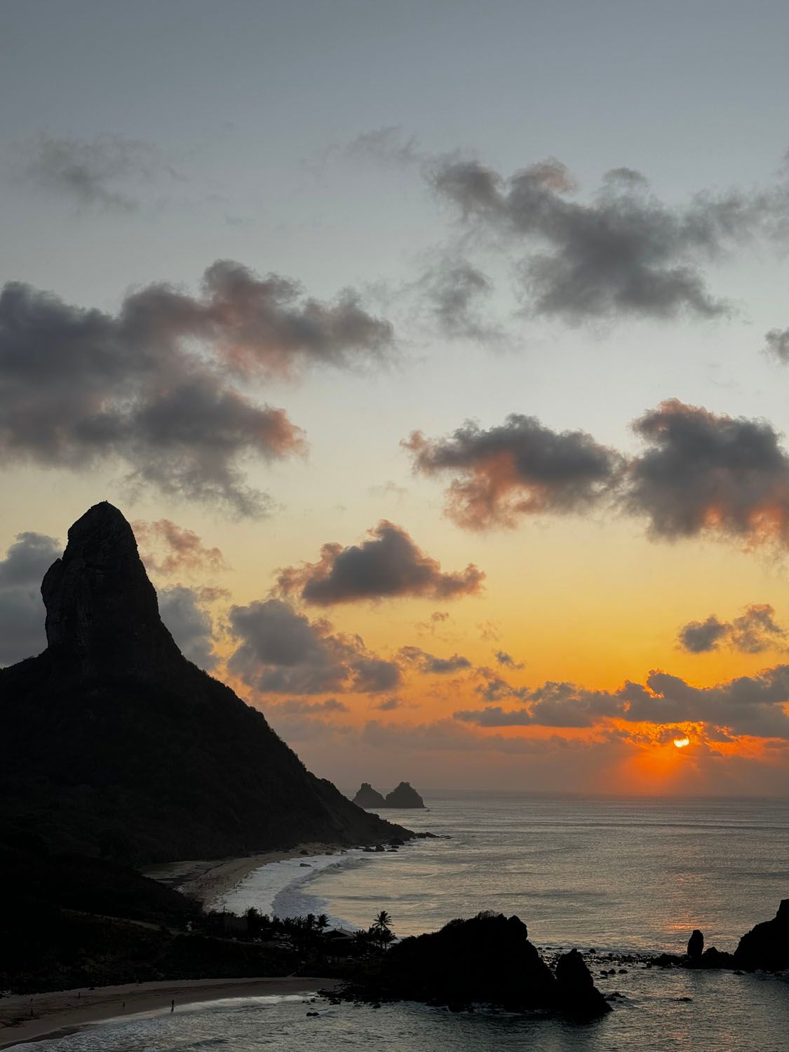 Um pôr do sol sobre o oceano com uma montanha em primeiro plano