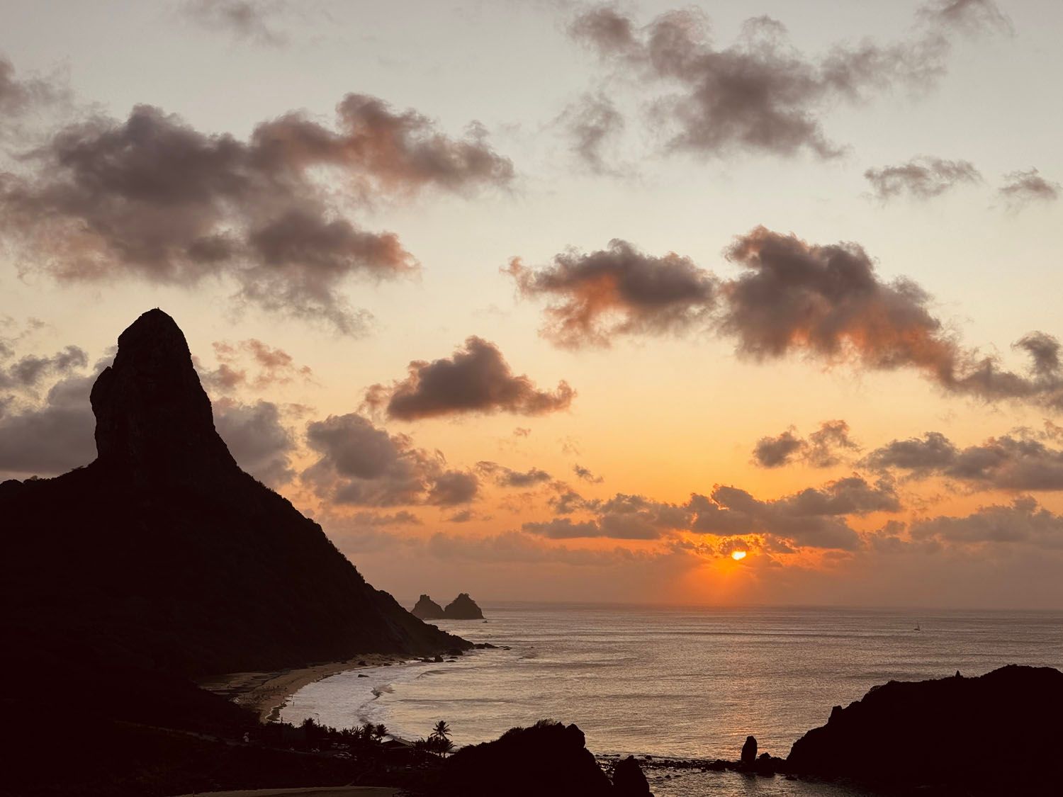 Um pôr do sol sobre o oceano com uma montanha em primeiro plano