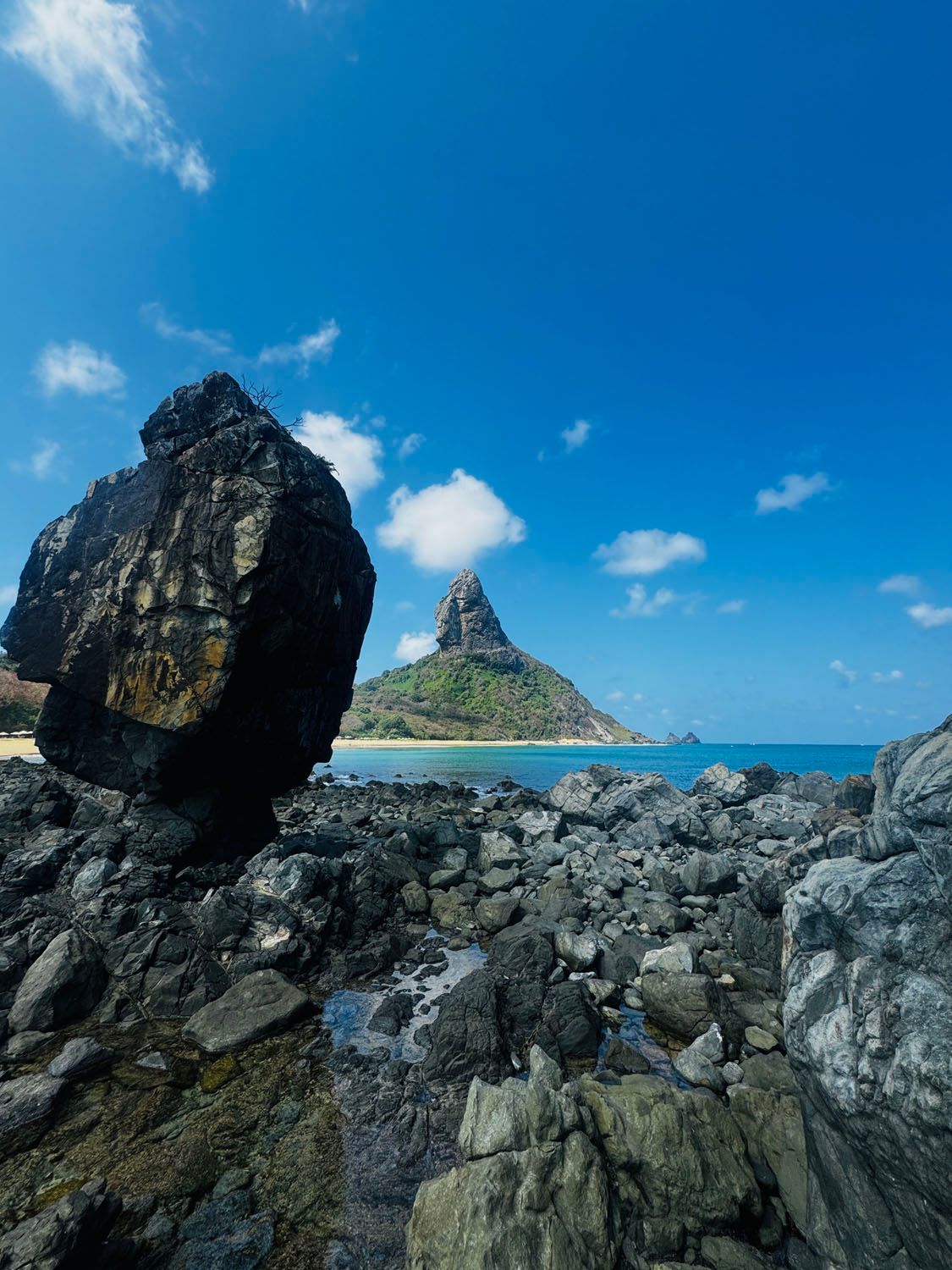 Uma costa rochosa com uma pequena ilha ao fundo e uma grande rocha em primeiro plano.