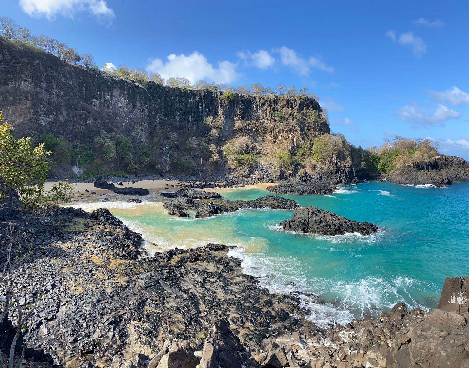 Uma vista de uma praia de um penhasco rochoso com vista para o oceano.