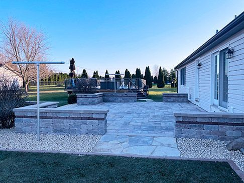 A large backyard patio with natural stone pavers, built-in seating walls, and elegant hardscaping. The outdoor space is perfect for relaxation and entertaining.