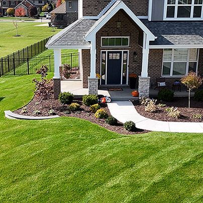 A beautifully designed front yard featuring a curved concrete walkway leading to a modern brick home with a covered porch. The landscaping includes vibrant plants, decorative mulch beds, and a well-manicured green lawn, enhancing the home's curb appeal.