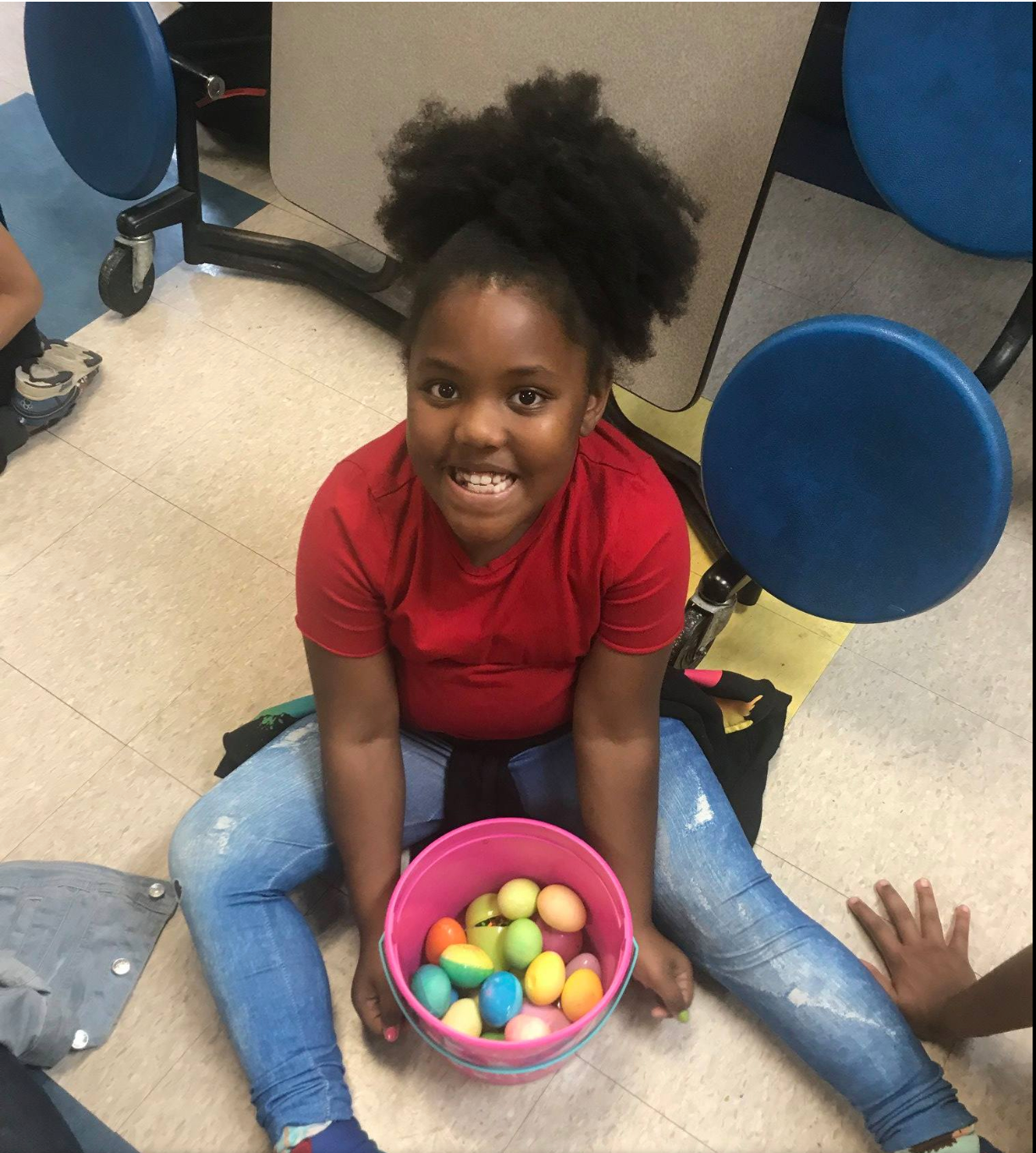 A little girl is sitting on the floor holding a bowl of easter eggs