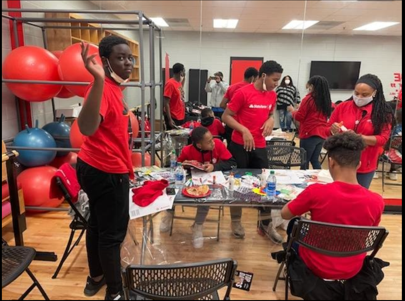 A group of people in red shirts are standing around a table in a gym.