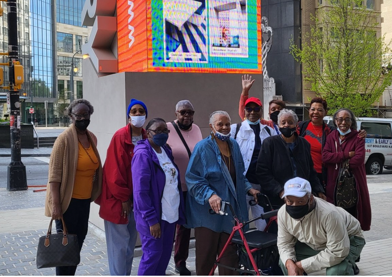 A group of people wearing masks are standing in front of a large screen.