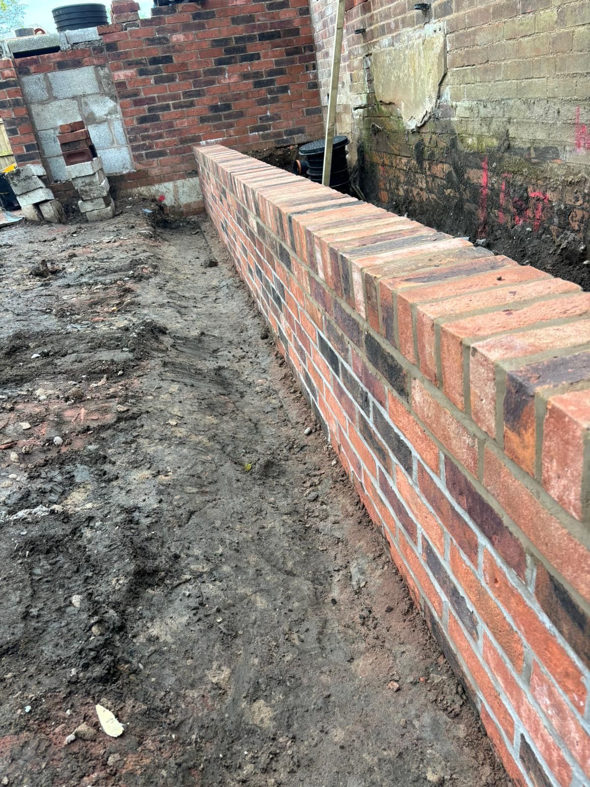 Newly constructed red brick wall next to muddy ground. Partially built brick structure visible in the background.