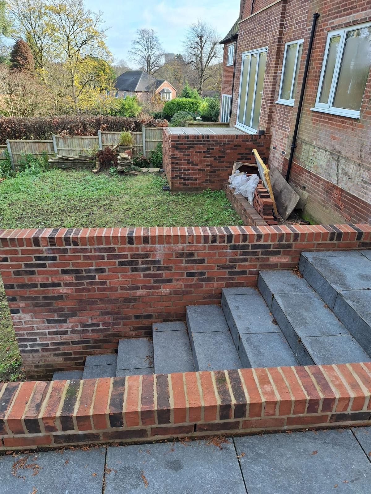 Brick retaining wall with stairs leading to a lower garden area. A house is visible in the background.