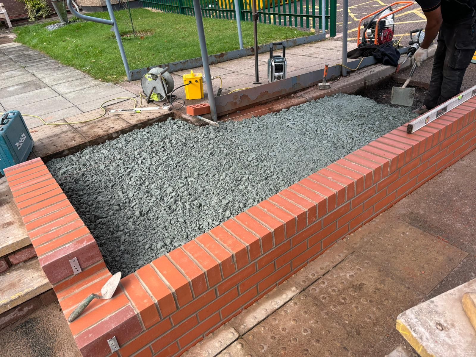 Brick planter with gravel filling, under construction by a person in work clothes, outdoor setting.