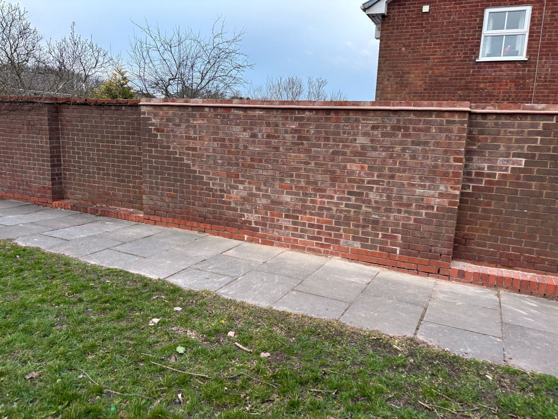 Red brick wall alongside a gray paved walkway and green grass.