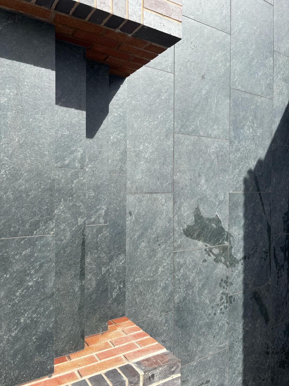 Dark stone wall with brick accents; sunlight casts shadows.