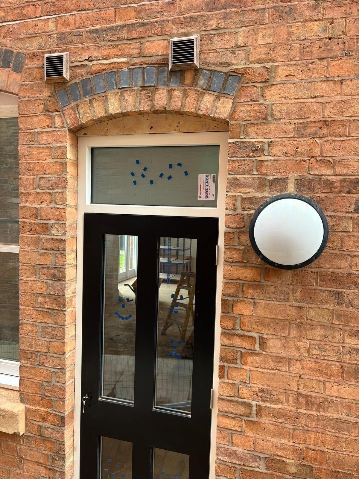 Black door in brick archway, with glass panels. A round white light is on the right.