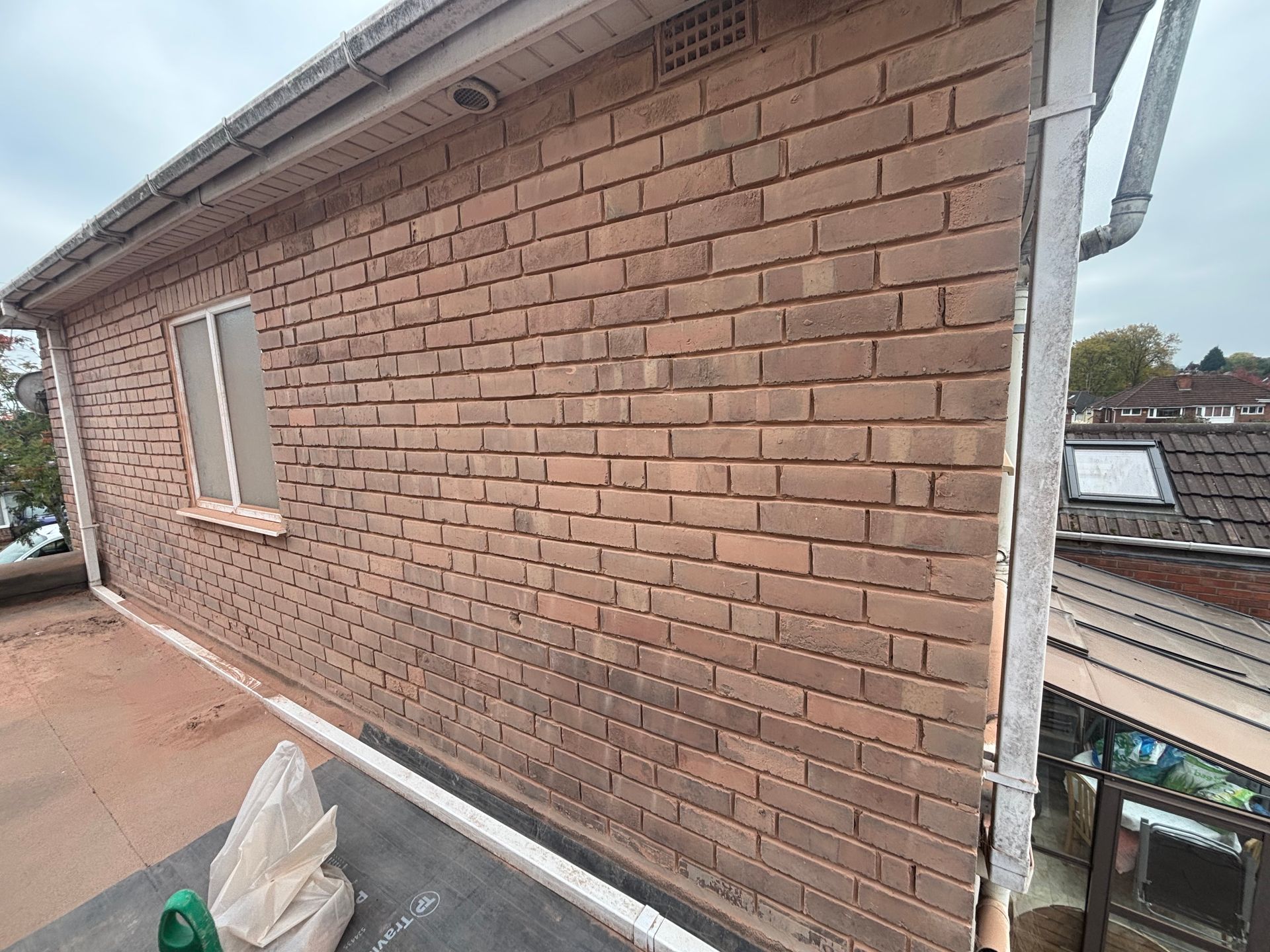 Brick building exterior with window, gutter, and flat roof.