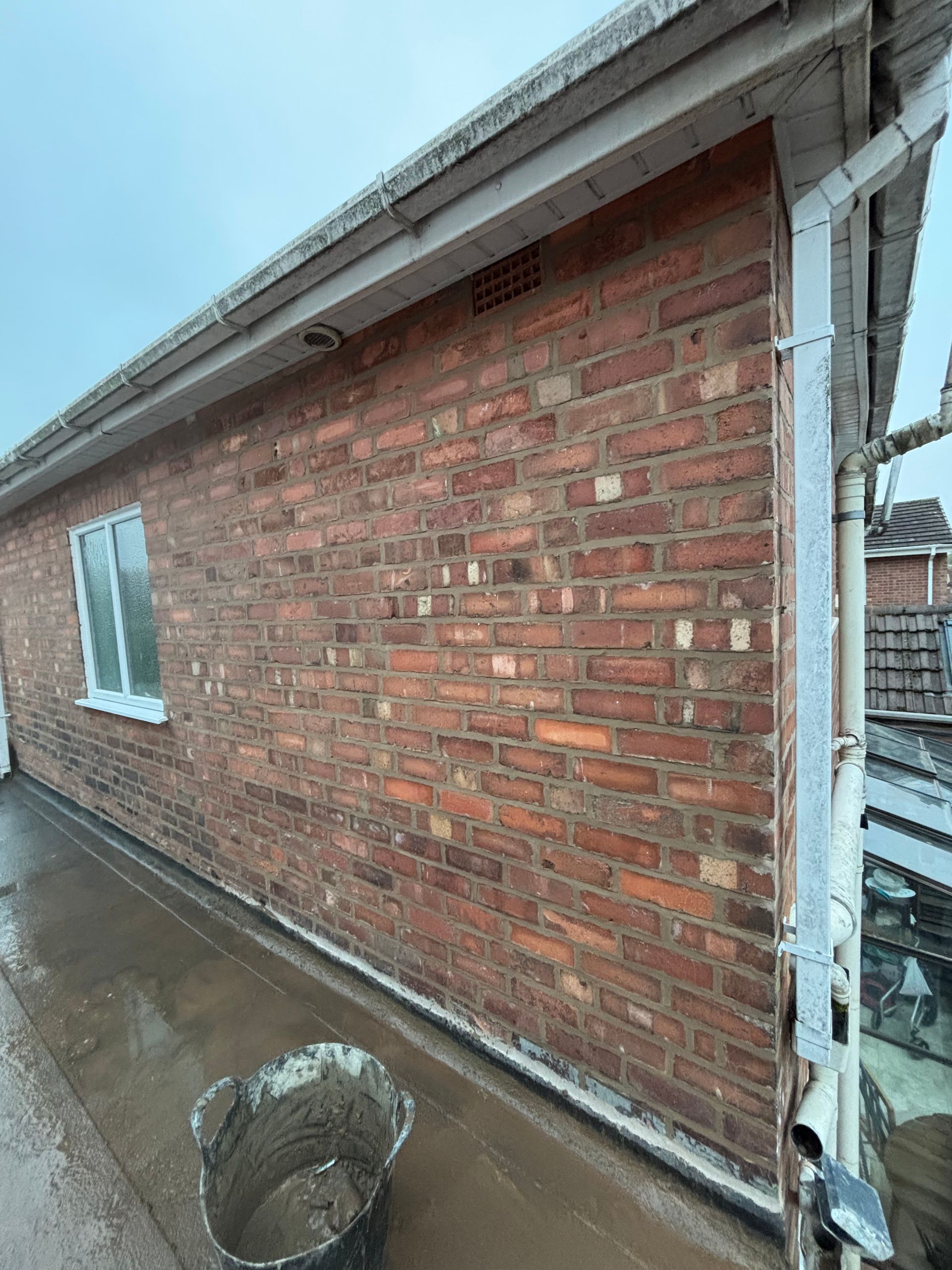 Brick building exterior with window, gutter, and a bucket of material.