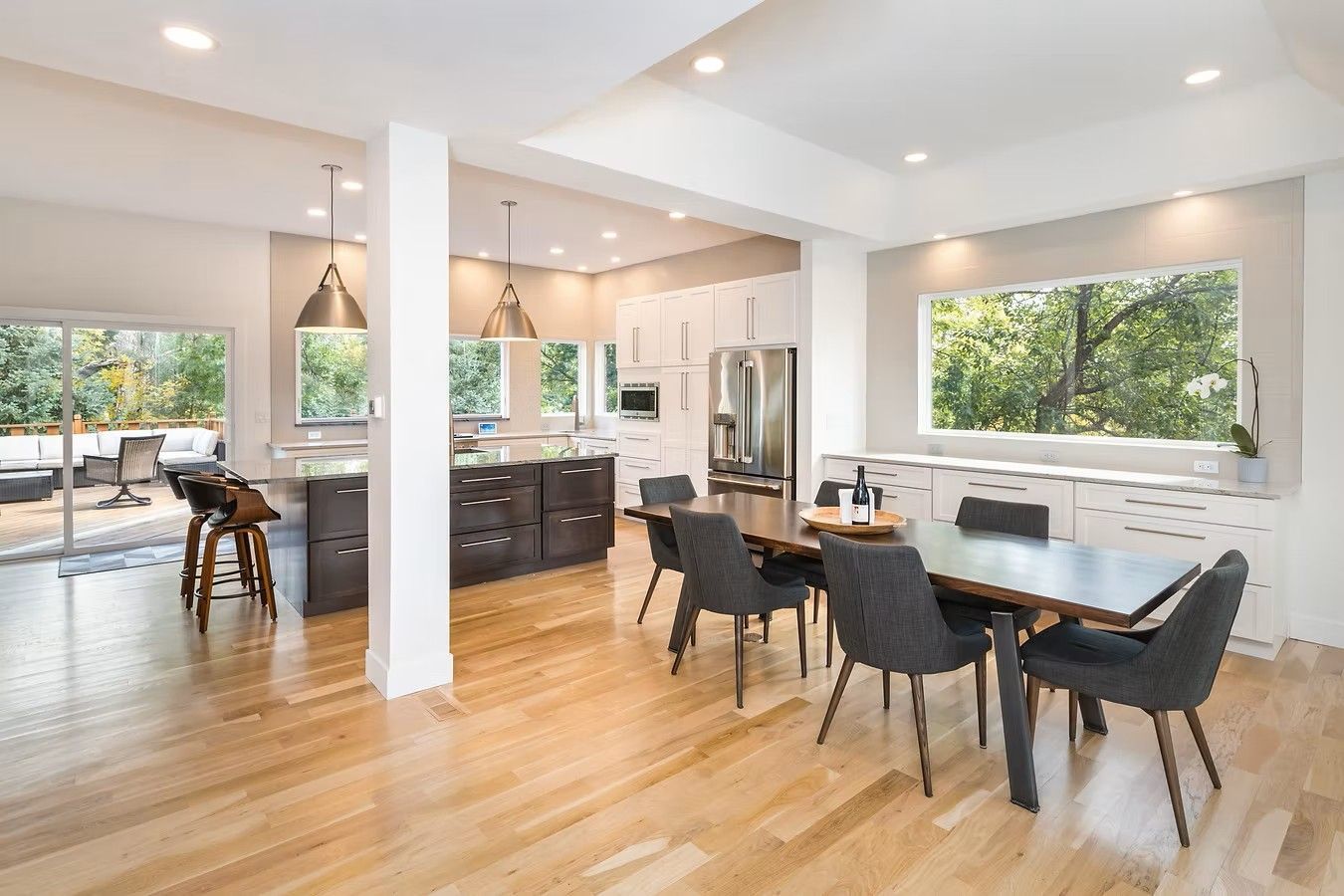 Bright open-concept kitchen and dining area with hardwood floors, dark cabinets, and large windows.