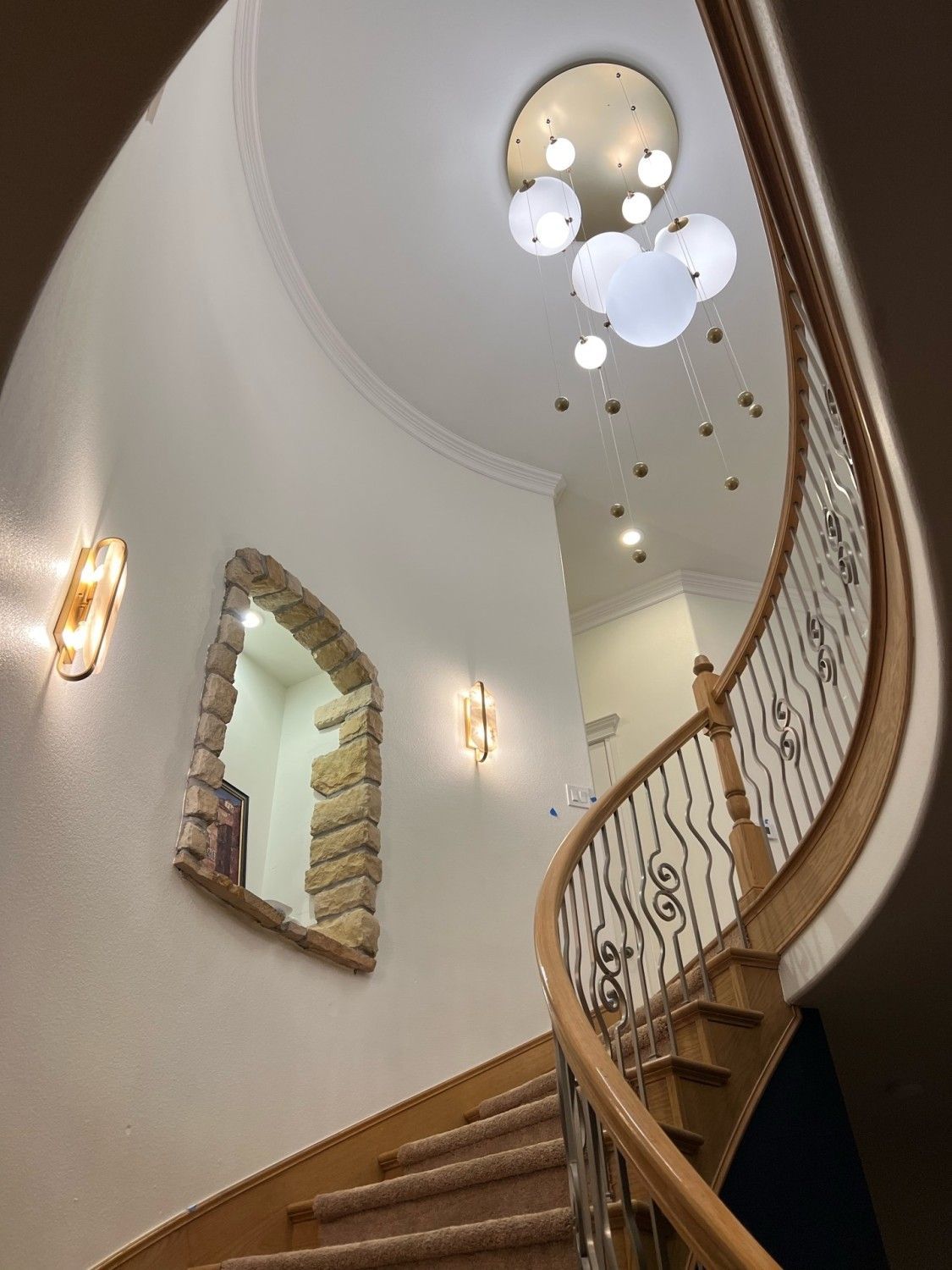Curving wooden staircase in a home with stone window frame, wall sconces, and globe chandelier.