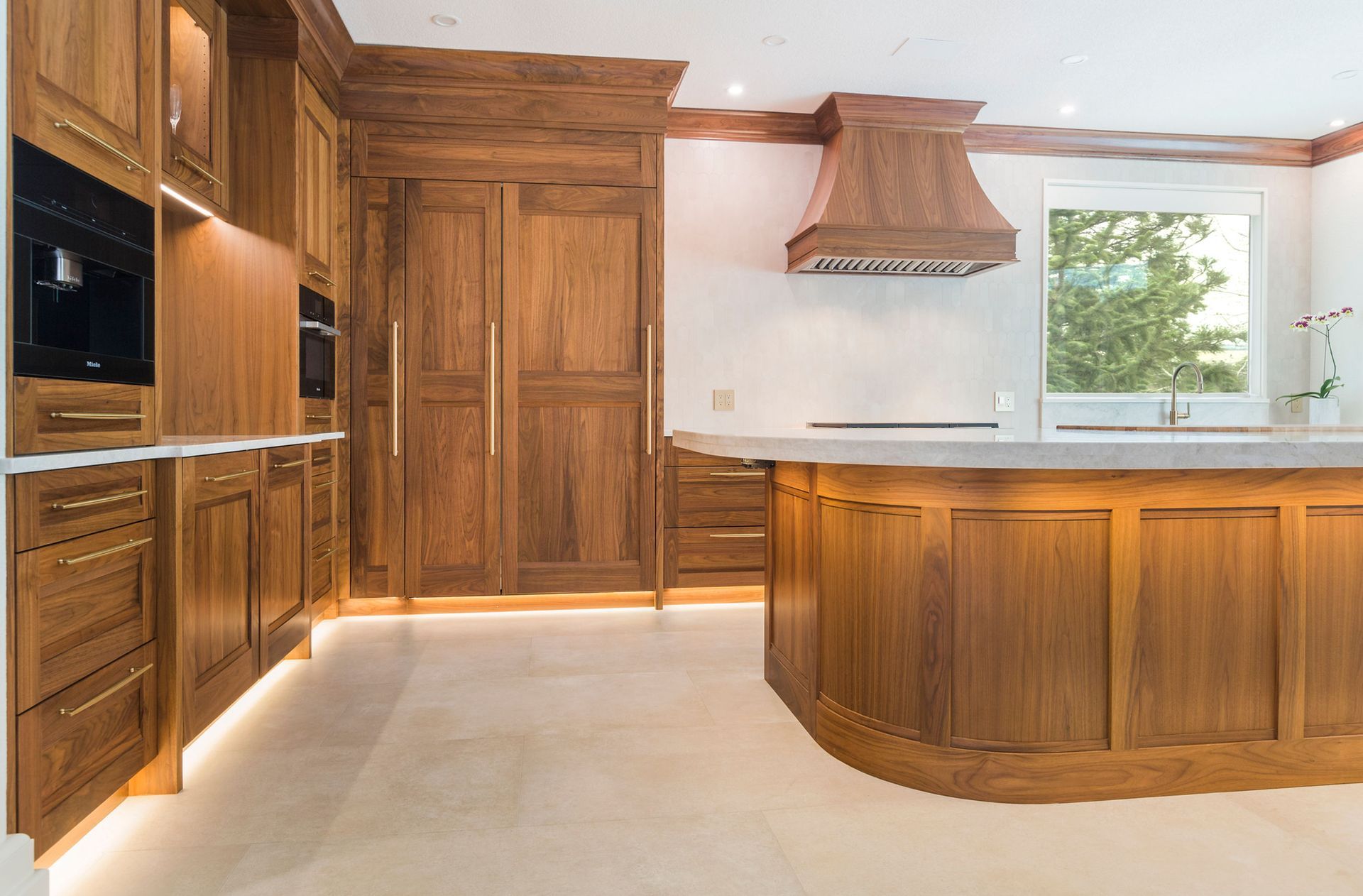 A kitchen with wooden cabinets, a central island, and a range hood. The space is light and airy.