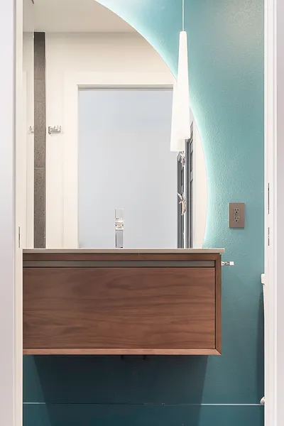 Floating wooden vanity in modern teal bathroom with backlit mirror.
