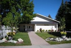 White building with angled roof, sidewalk leading to door, surrounded by greenery.