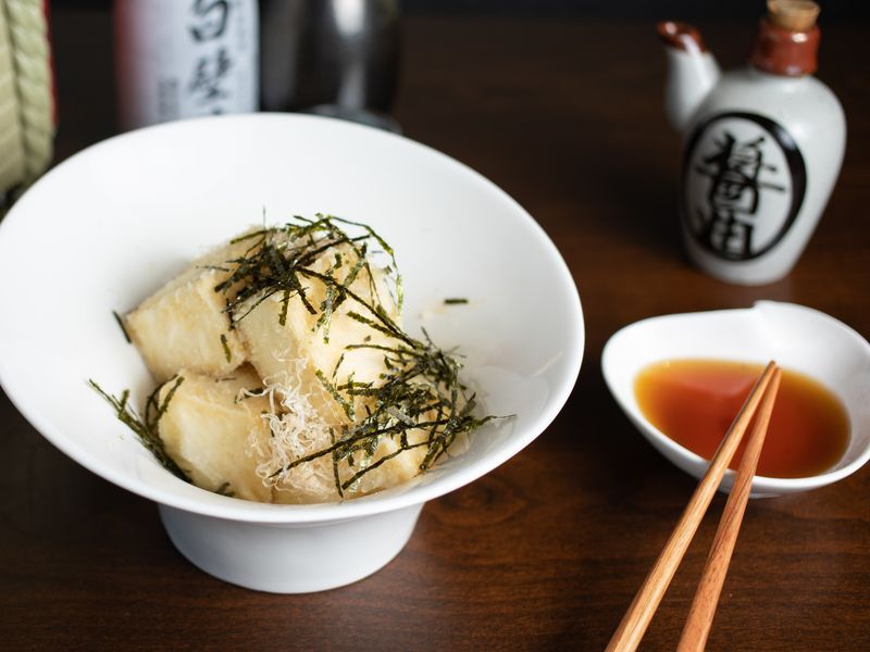 A bowl of food with chopsticks next to a bowl of dipping sauce