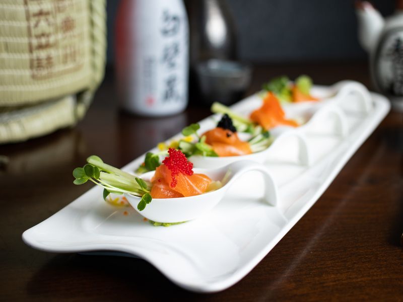 A close up of a plate of food on a table with a bottle of sake in the background.