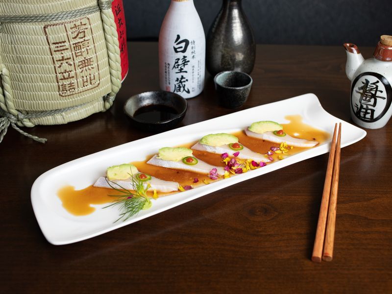 A plate of food with chopsticks and a bottle of sake in the background