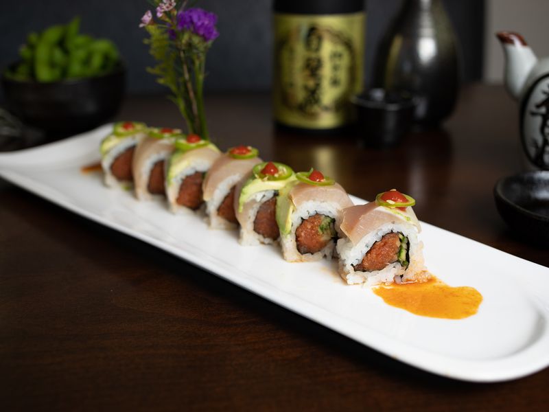 A row of sushi rolls on a white plate on a table.