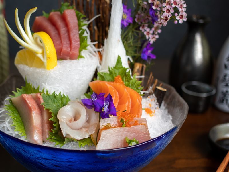 A blue bowl filled with different types of sashimi on ice.