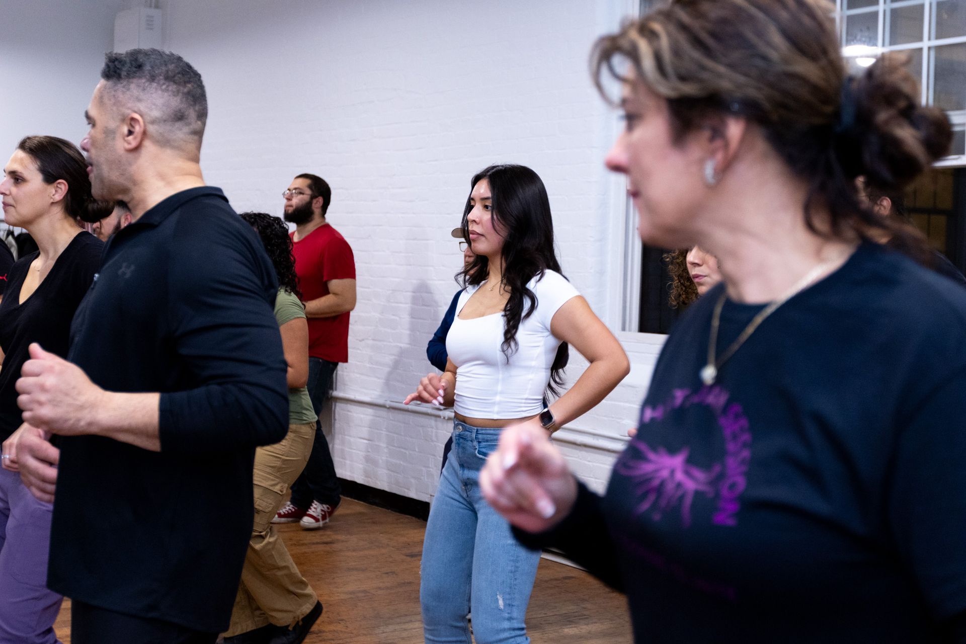 A group class of younger and older men and women practice footwork during a Bachata class. 