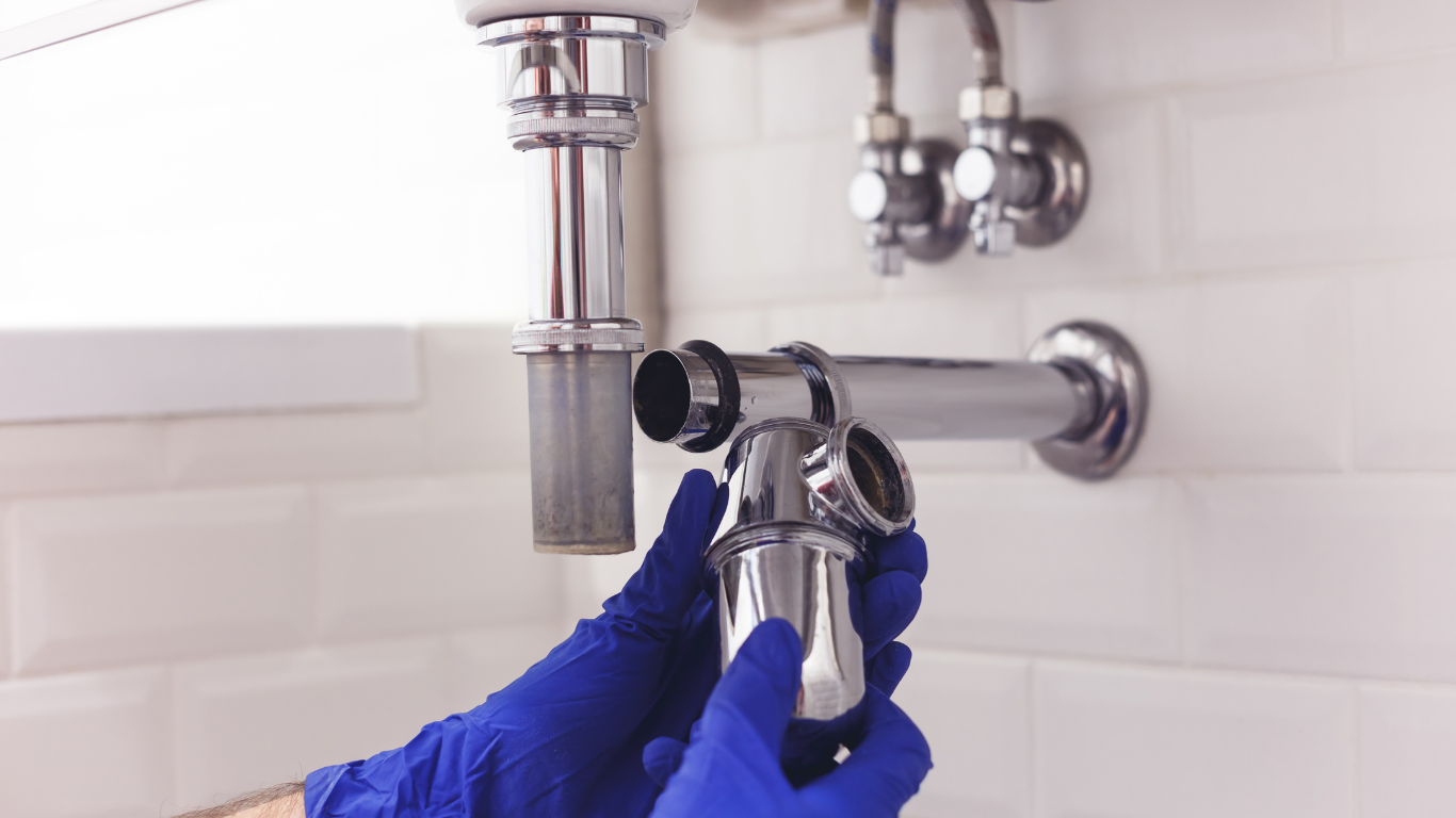 Blue-gloved hands installing a chrome faucet in a white-tiled sink area