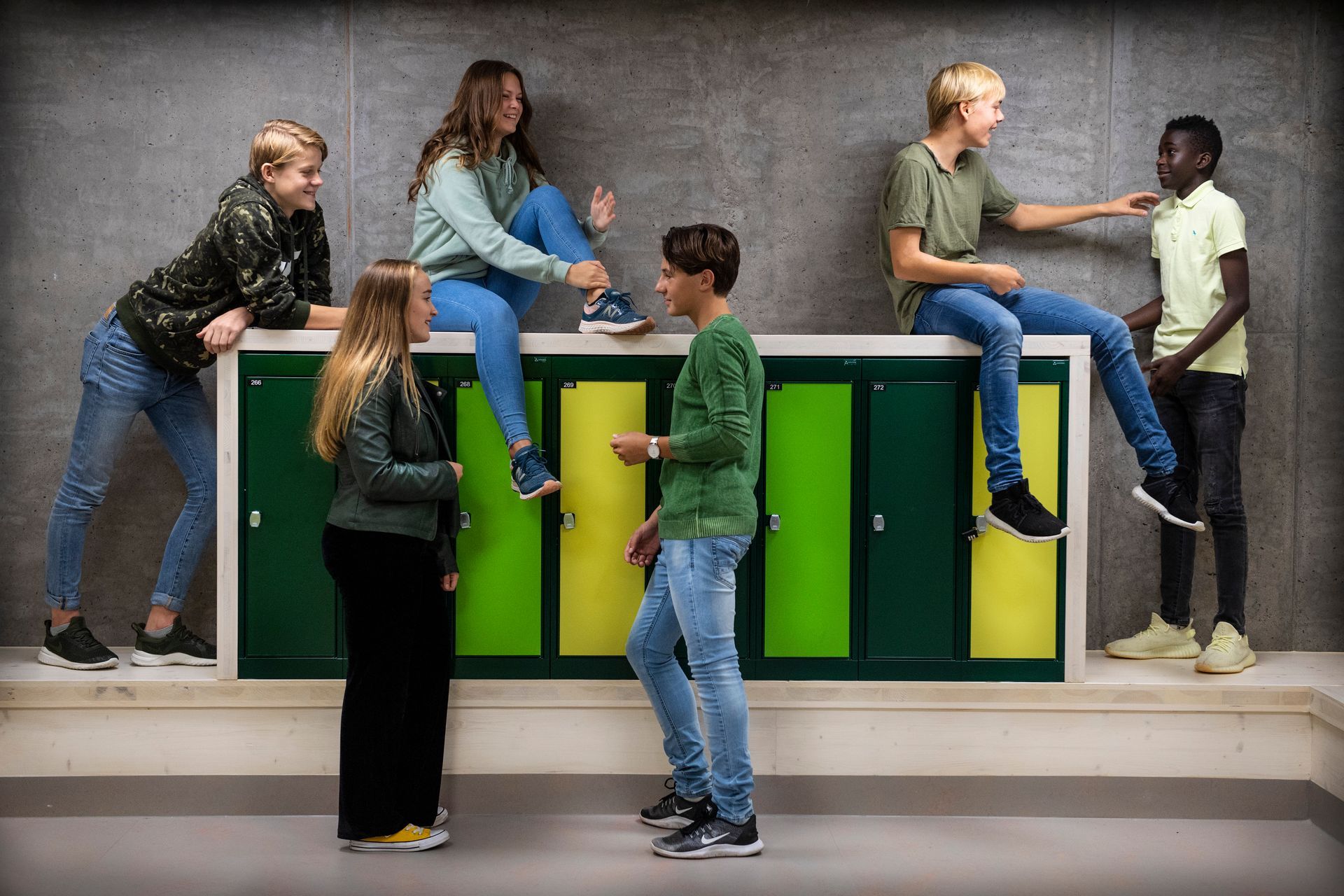 Gruppe tenåringer samhandler i nærheten av grønne skap mot en grå vegg.