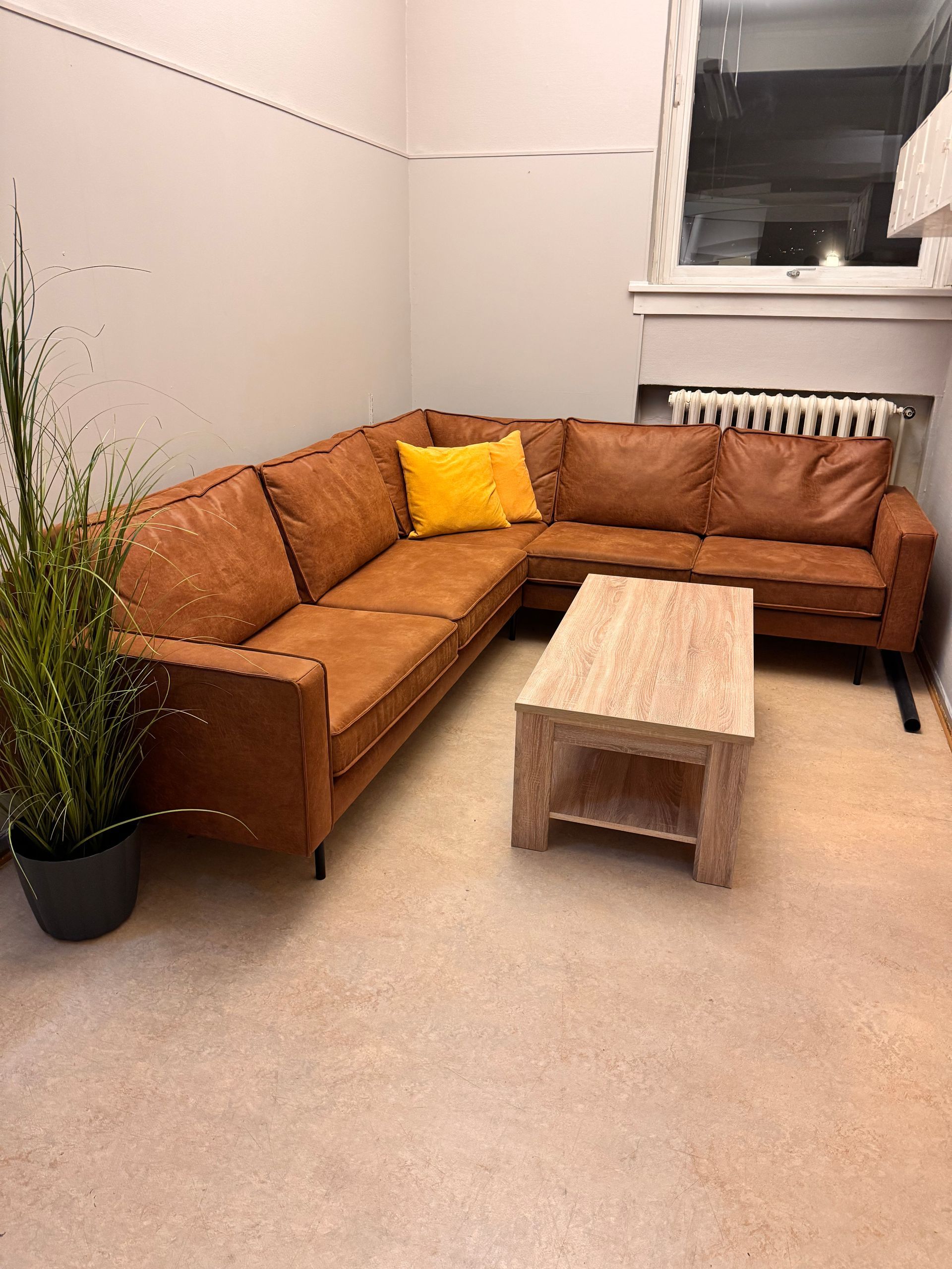 Brun skinnseksjonssofa med gul pute og salongbord i tre i et rom.