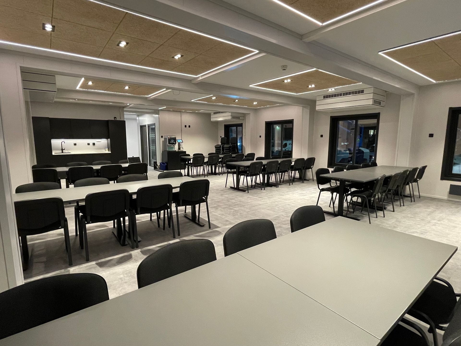 Konferanserom med svart bord, oransje stoler og et kjøkkenområde med grå skap og en stor potteplante.