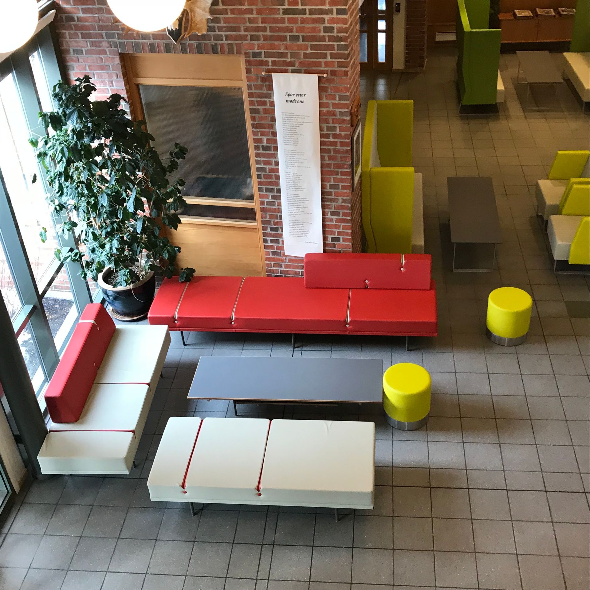 Ovenfra-bilde av en lobby med røde, grå og hvite modulære sitteplasser, murvegger og potteplanter.